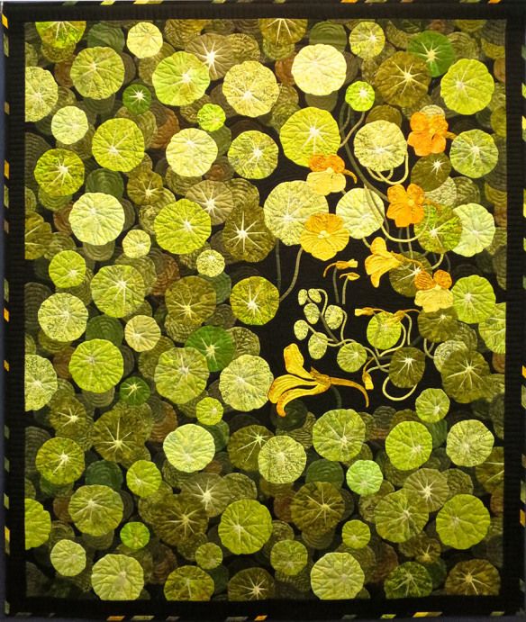 a quilt made with green and yellow leaves on black fabric, featuring an image of water lilies