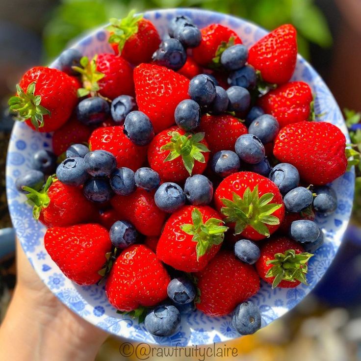 a blue and white bowl filled with strawberries and blueberries