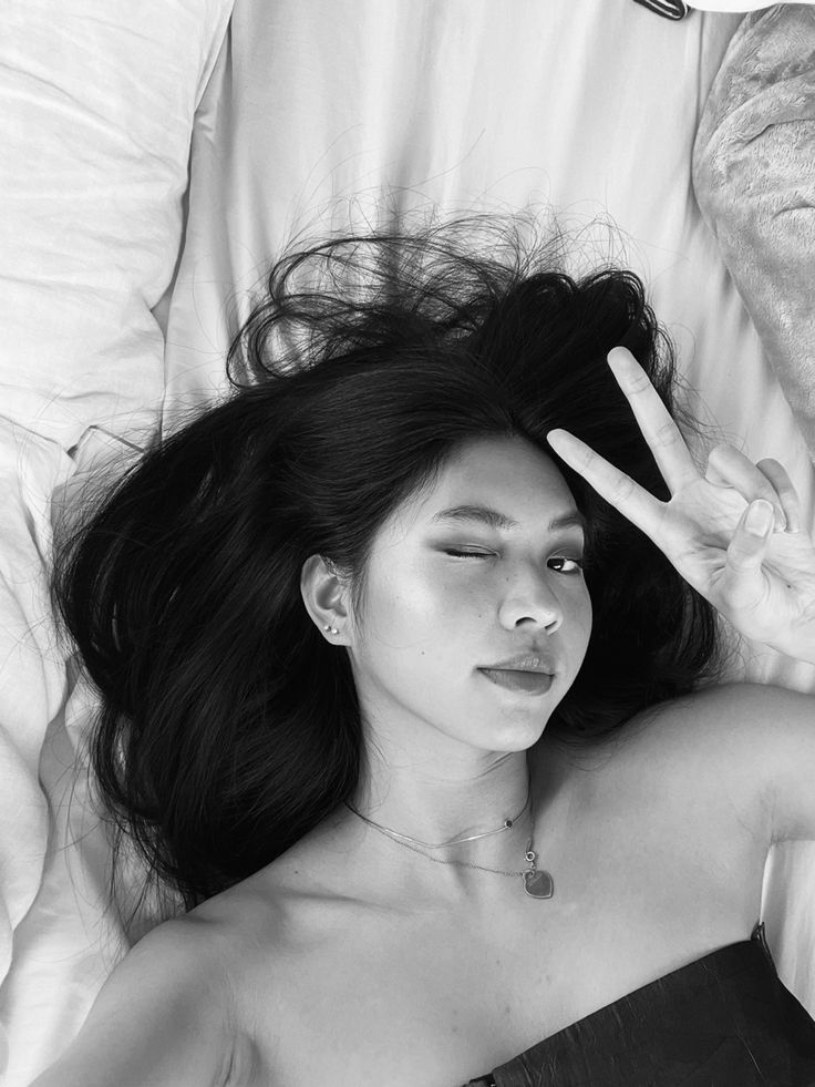 a woman laying in bed making the peace sign with her hand while wearing a strapless dress