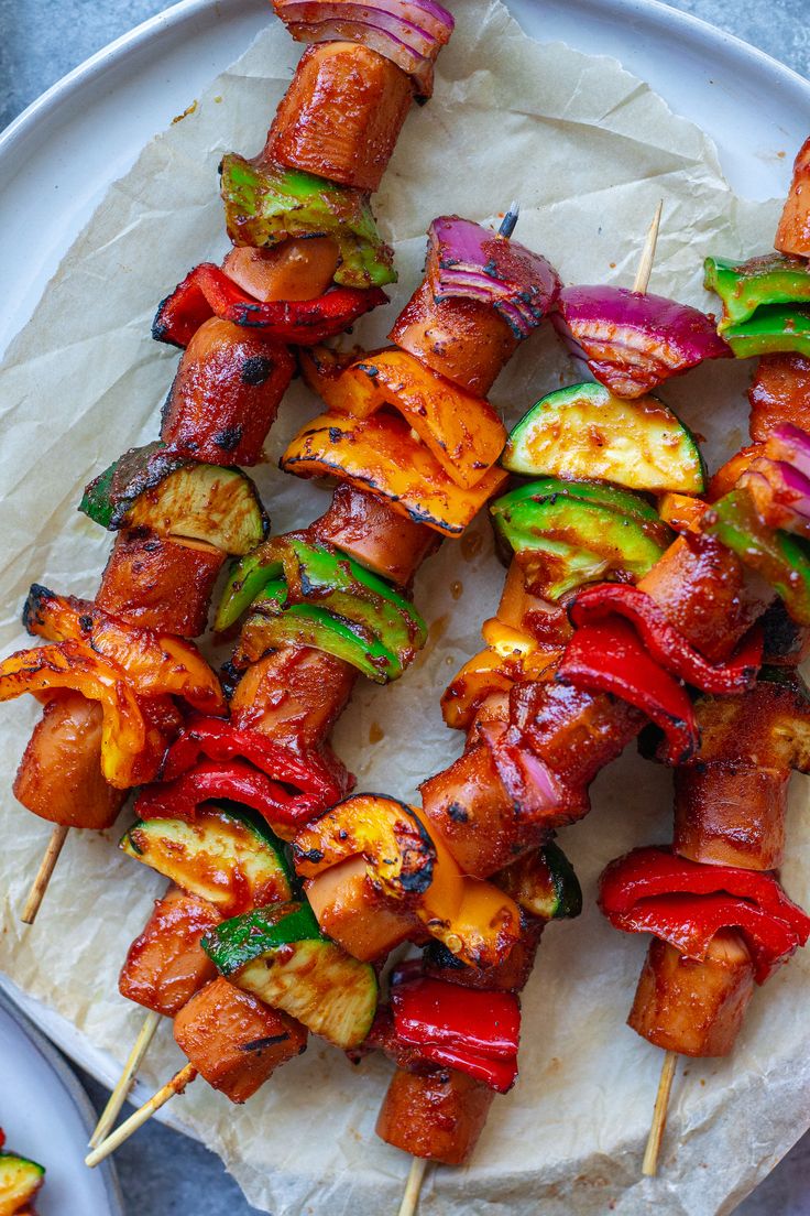 several skewers of meat and vegetables are on a white plate with parchment paper