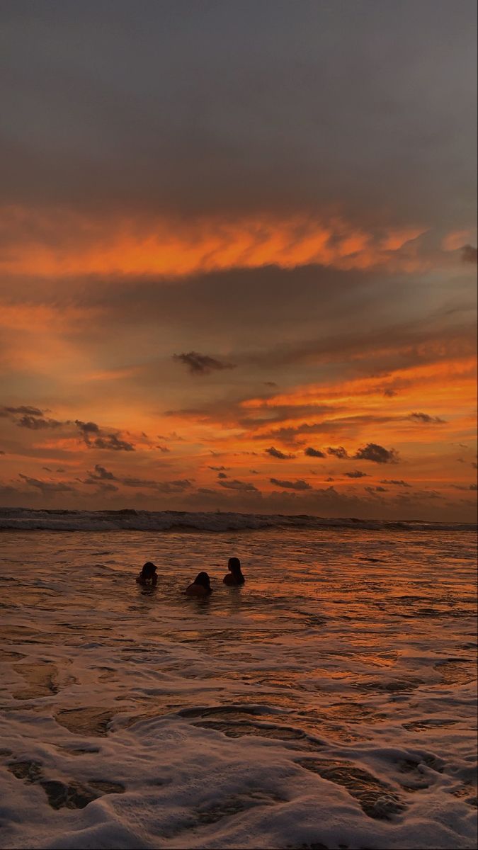 two people swimming in the ocean at sunset