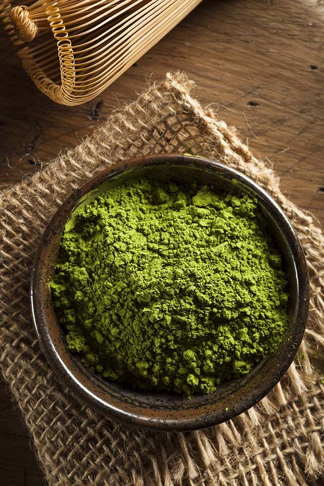 a bowl filled with green powder sitting on top of a wooden table next to a wicker basket