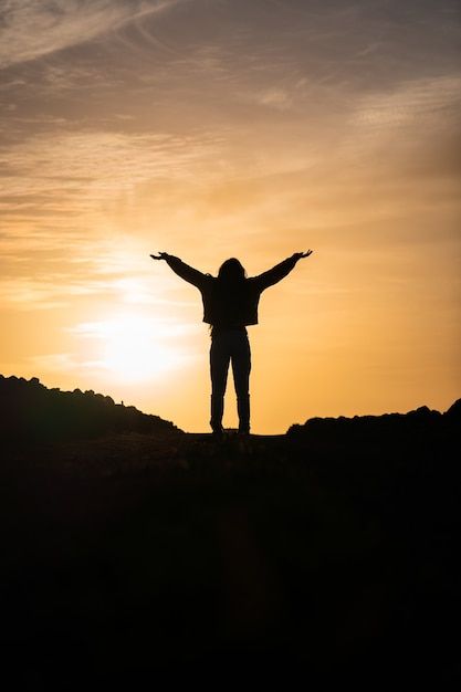 a person standing on top of a hill with their arms wide open in front of the sun