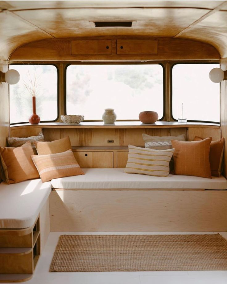 the inside of a camper with lots of windows and pillows on the seat area