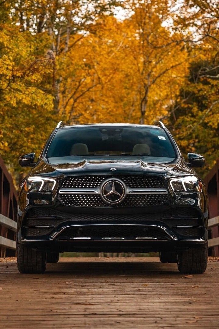 the front end of a black mercedes gle parked on a wooden bridge with trees in the background