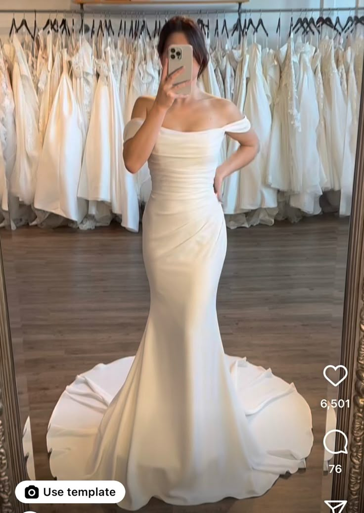 a woman taking a selfie in front of a mirror wearing a white wedding dress