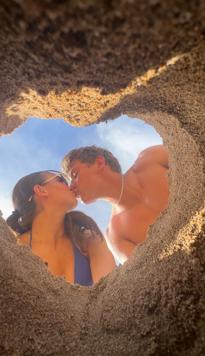 a man and woman are kissing in the shape of a heart made out of sand