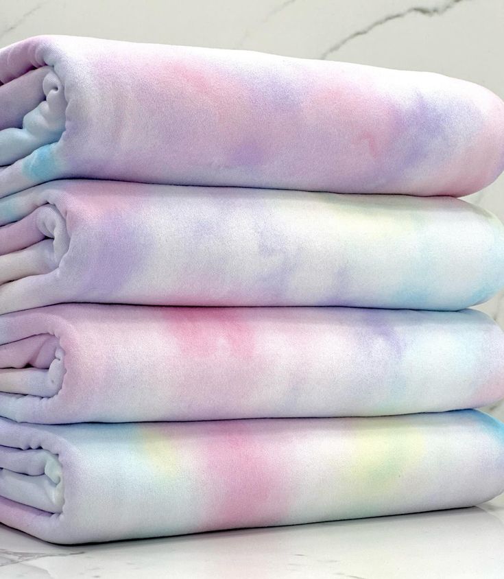 three blankets are stacked on top of each other in pastel colors, one is pink and the other is blue