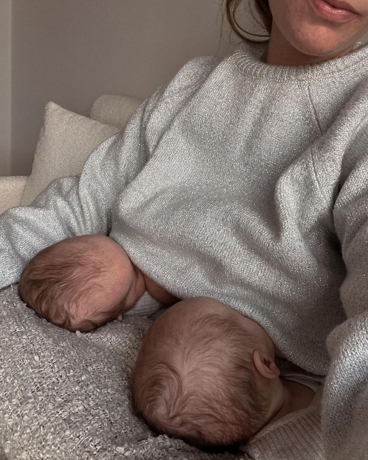 a woman holding two babies in her arms on a couch with the baby's head resting on its mother's shoulder