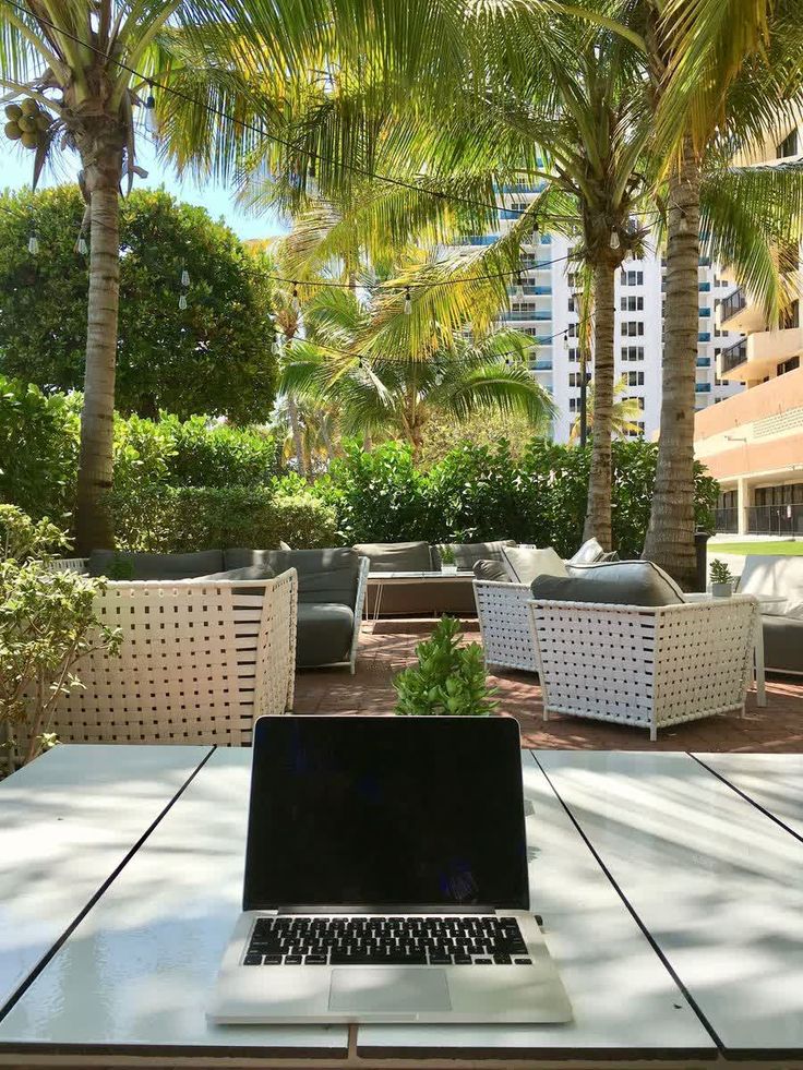 an open laptop computer sitting on top of a wooden table next to chairs and palm trees