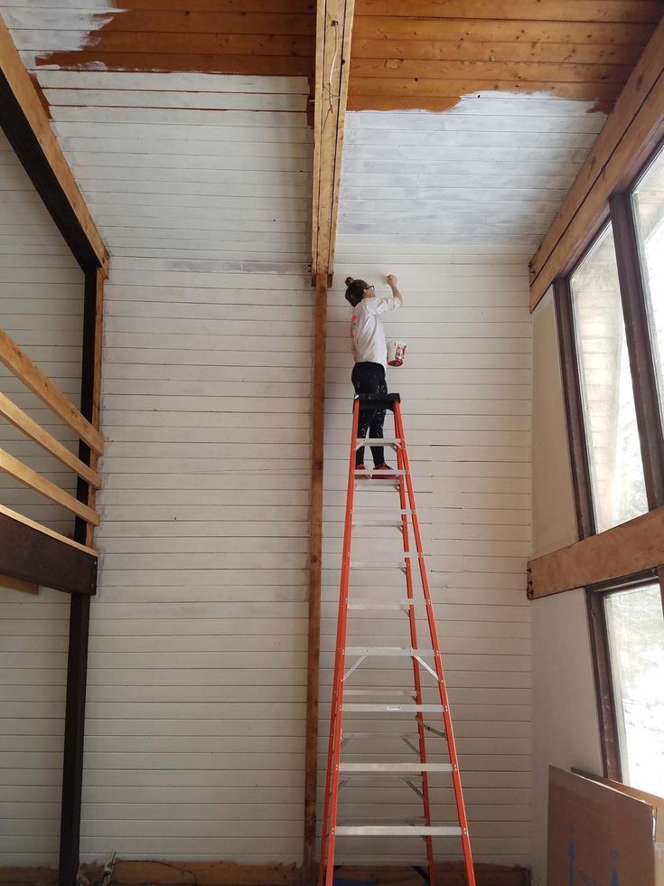 a woman standing on a ladder painting the ceiling