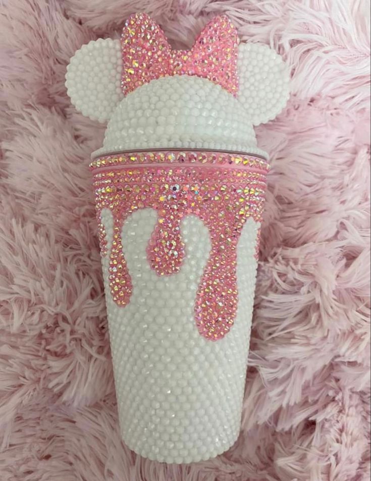 a white cup with pink bows and sequins on it sitting on a furry surface