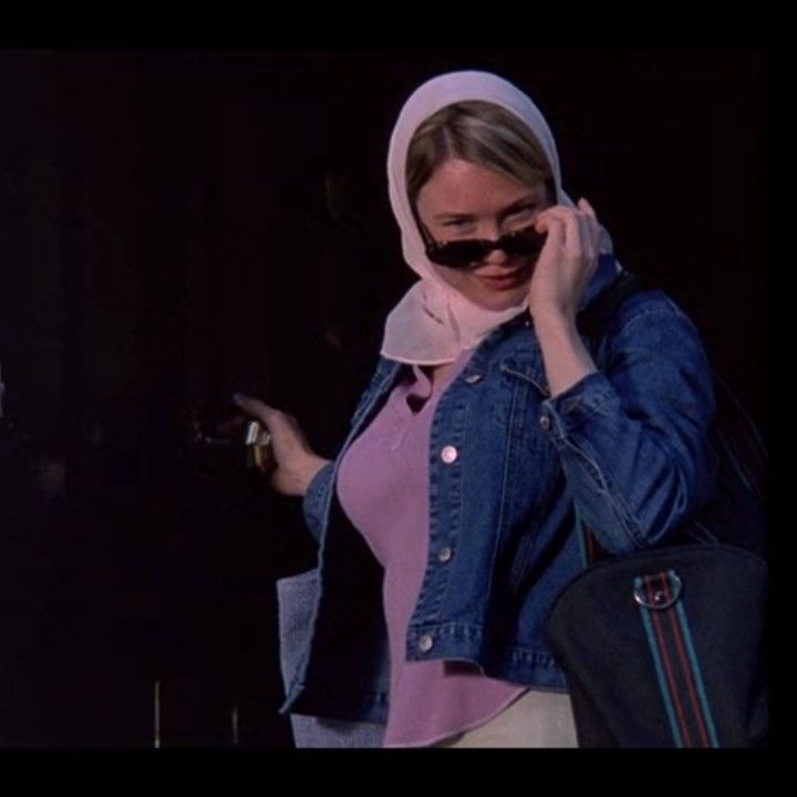 a woman in a pink top and jean jacket is talking on her cell phone while holding a black purse