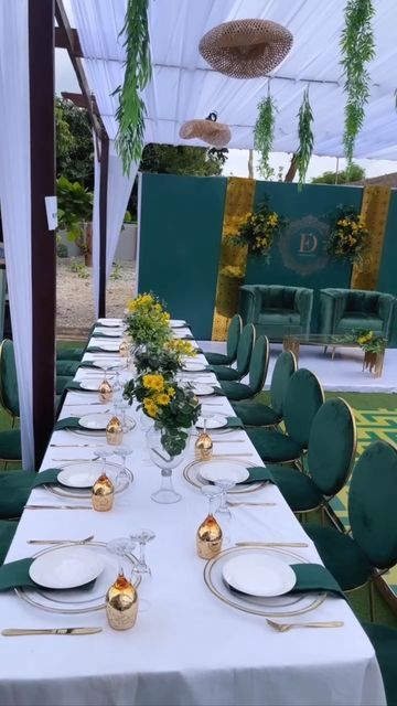 a long table is set with green chairs and white tablescloths, gold place settings and yellow flowers