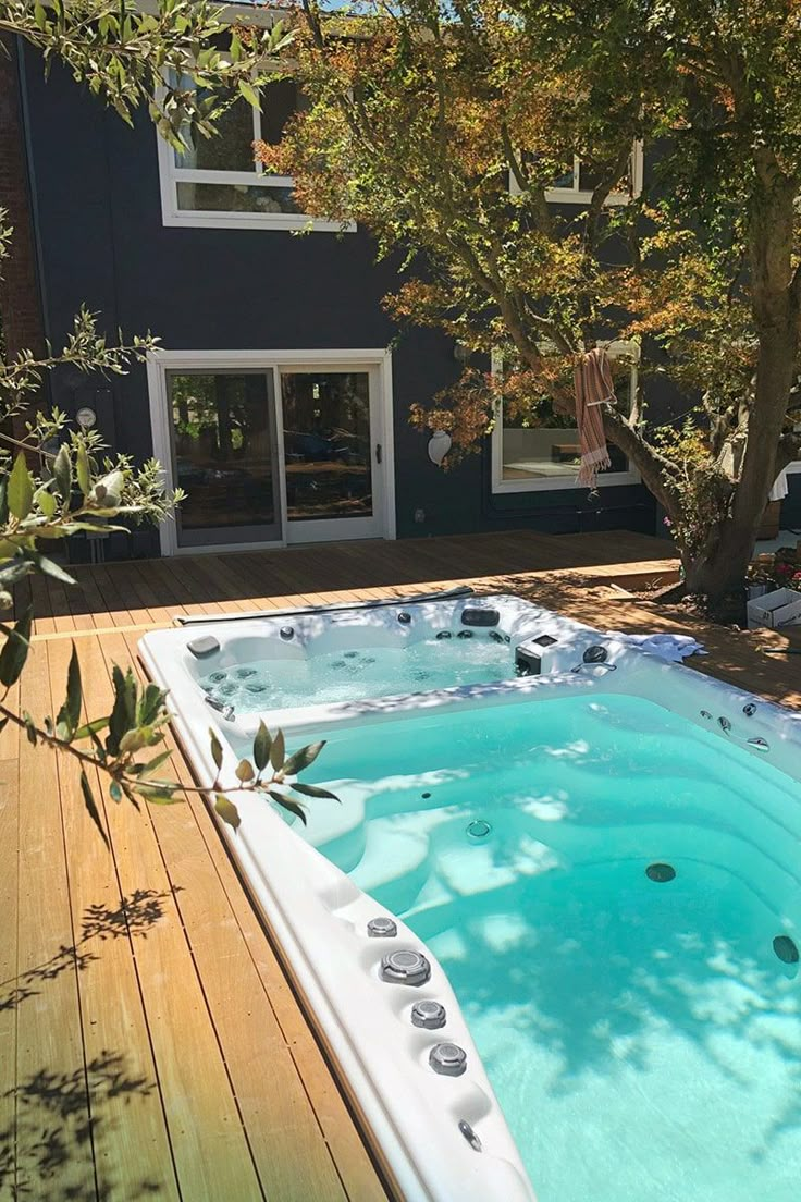 a large hot tub sitting on top of a wooden deck next to a tree in front of a house