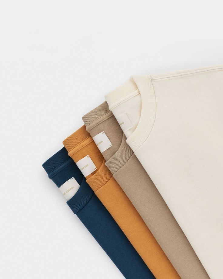 four different colors of t - shirts on a white surface with one folded up and the other closed