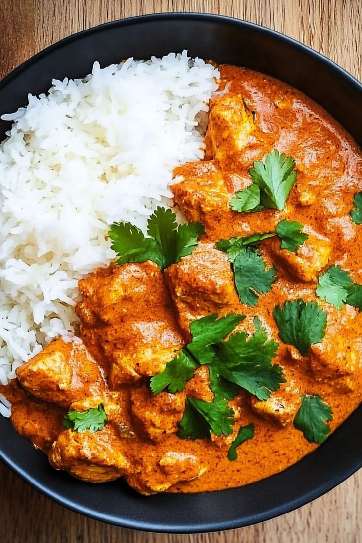 a black bowl filled with rice and chicken curry next to cilantro garnished with parsley