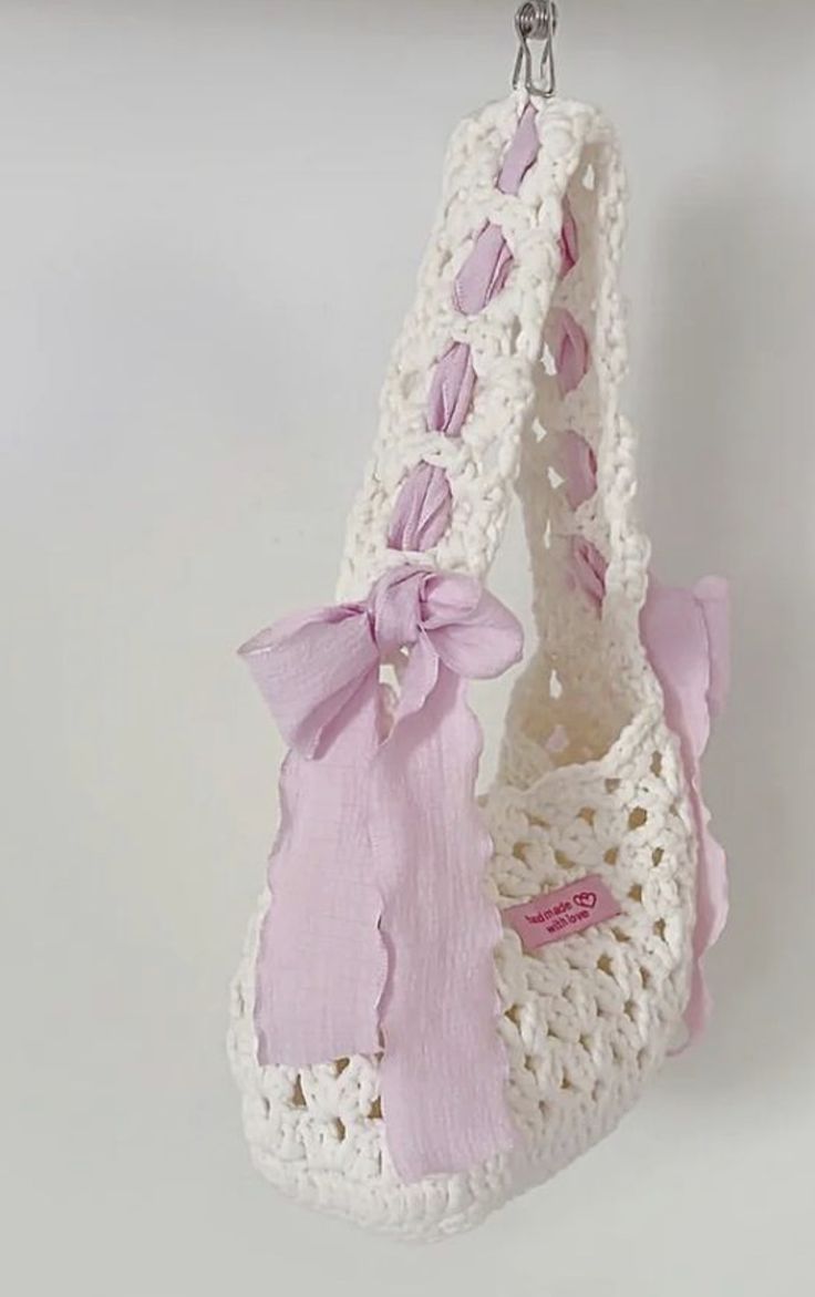 a crocheted purse hanging from a hook with a pink bow on the handle