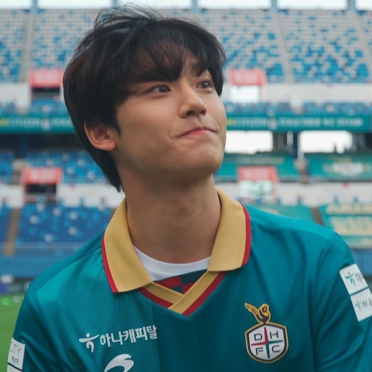 a young man standing in front of a stadium filled with blue and green seats looking up at the sky