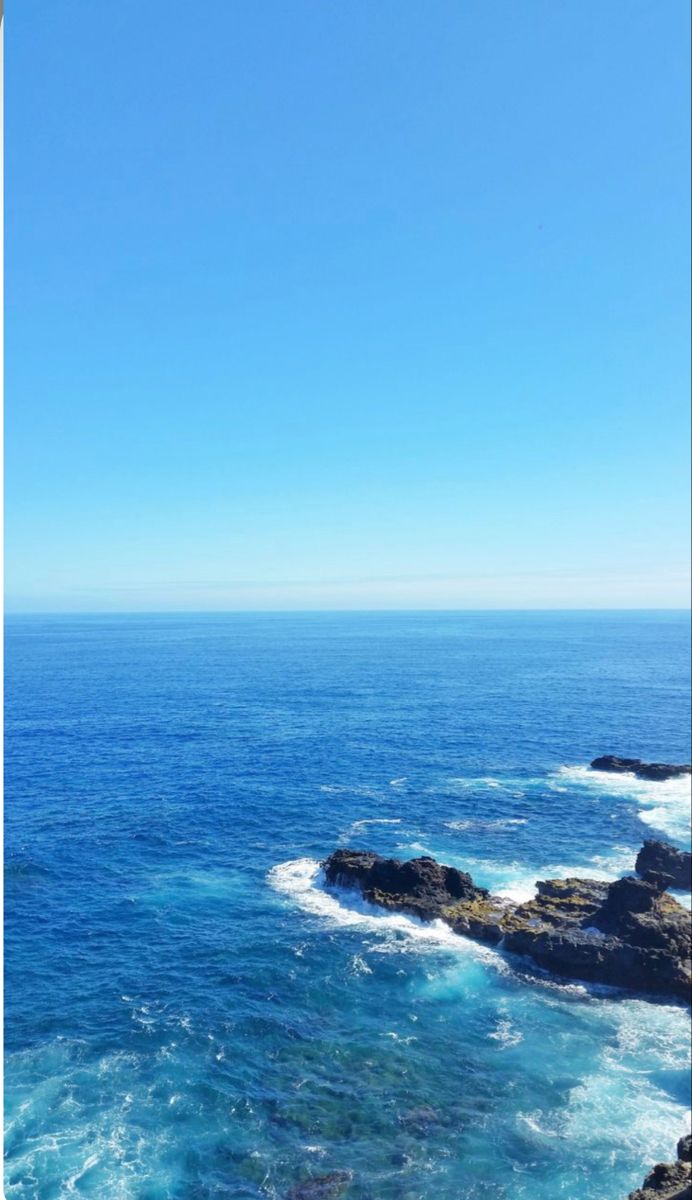 the ocean is blue with waves coming in from the shore and rocks on the shoreline