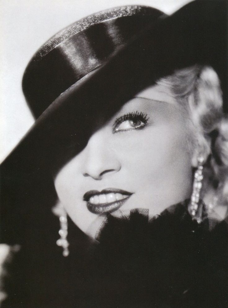 a black and white photo of a woman wearing a hat with pearls on her ear