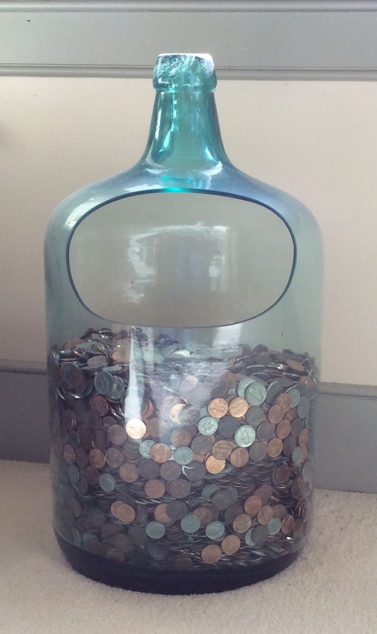 a glass bottle filled with coins sitting on top of a floor next to a wall