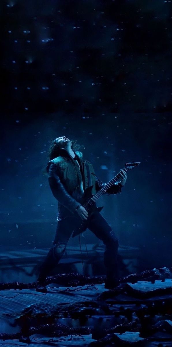 a man playing an electric guitar in the dark with snow falling all around him and on his knees