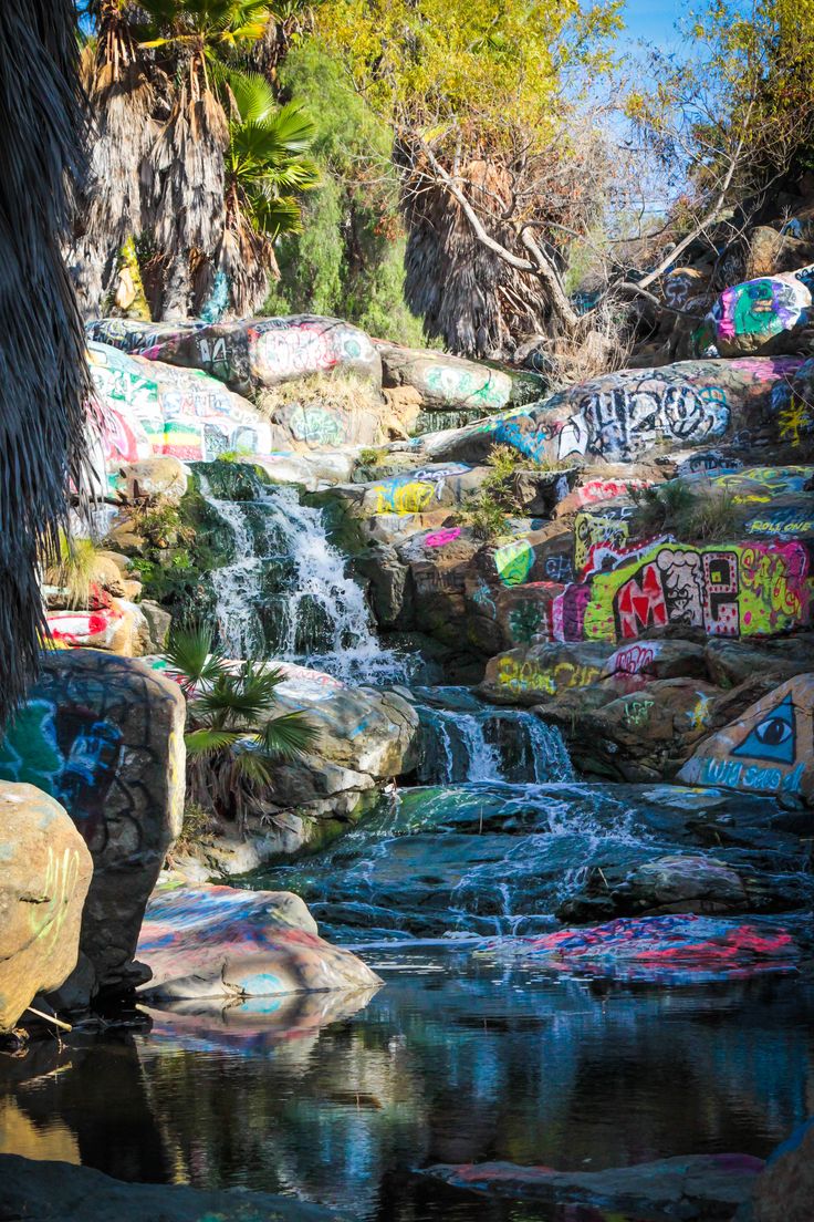 there is a waterfall that has been painted on the rocks and trees in the background