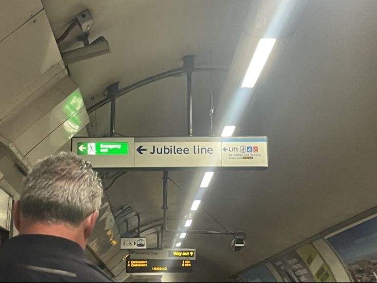 a man standing on a subway train next to a green and white sign that says jubilee line