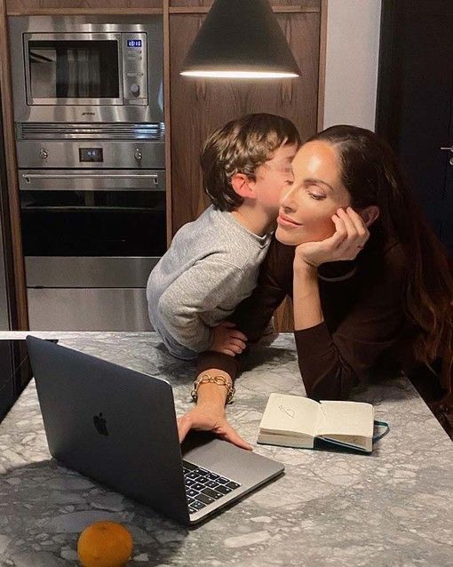 a mother kissing her son on the cheek while he works on his laptop in front of him