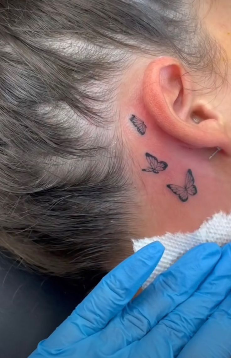 a woman's behind the ear tattoo with butterflies on her left side and right hand in blue gloves