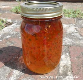 a glass jar filled with red liquid sitting on top of a stone floor next to grass