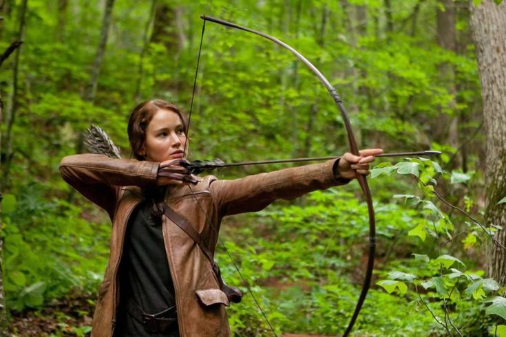 a woman in the woods aiming at an arrow with her bow and arrows on her chest