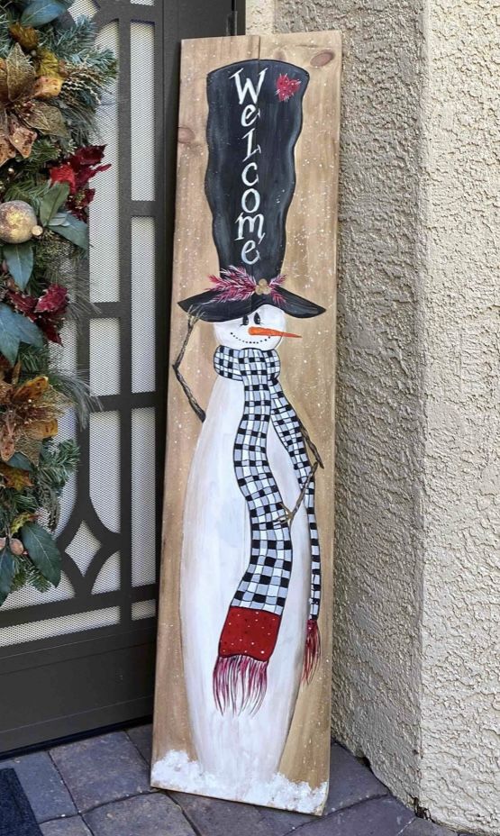 a wooden sign with a snowman wearing a hat and scarf on it's head