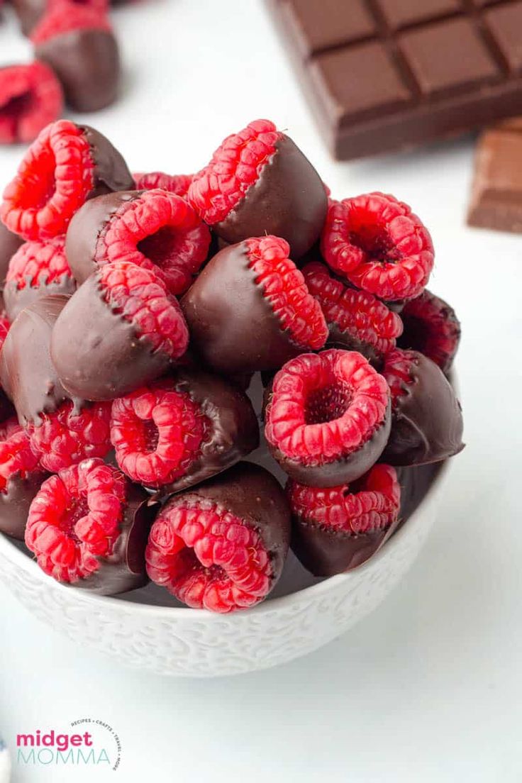 a white bowl filled with chocolate covered raspberries and surrounded by dark chocolate bars