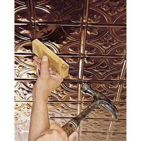 a person using a hammer to fix a tined metal ceiling tile in a home