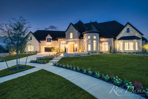 a large house that is lit up at night with the lights on and landscaping in front