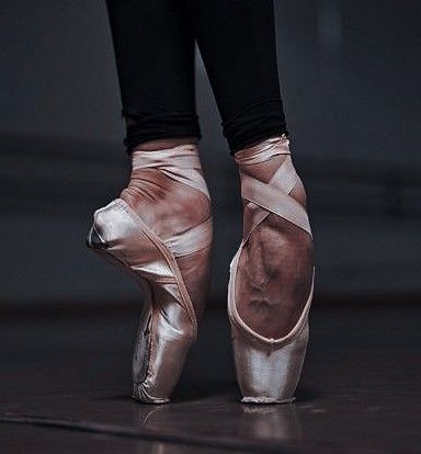 the feet of a ballerina in ballet shoes on a dark floor with reflections from them