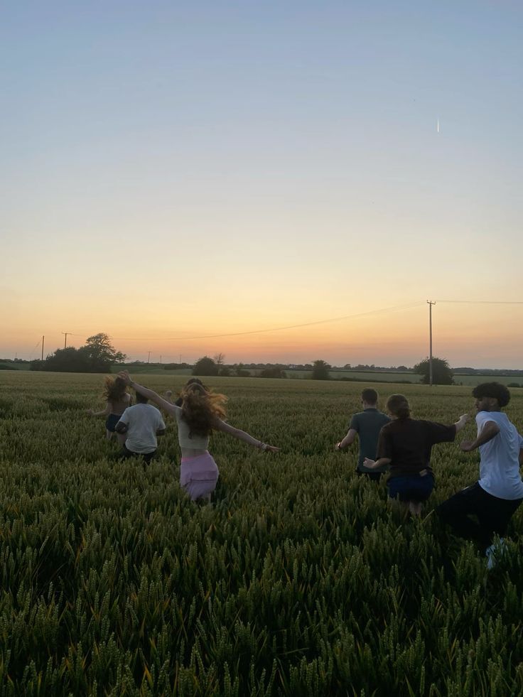 four people in a field with their arms outstretched and one person reaching out to the sky