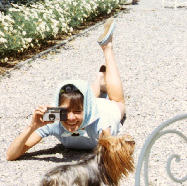 a woman laying on the ground with a dog and taking a photo in front of her