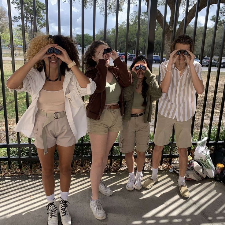 four girls are standing in front of a fence looking through binoculars