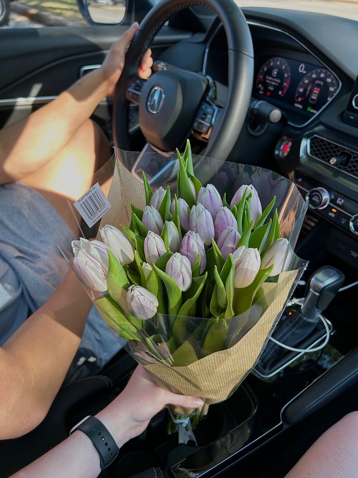 a person holding a bouquet of tulips in their hand while sitting in the driver's seat of a car