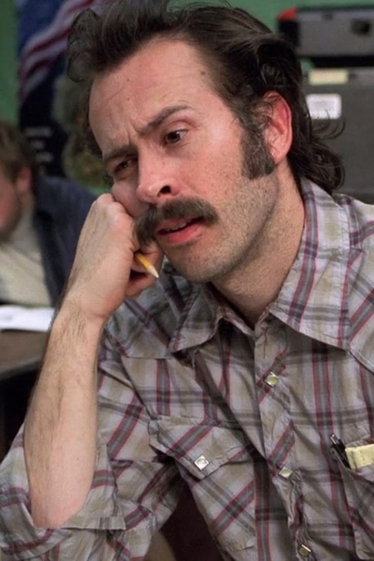 a man with a moustache on his face talking on a cell phone in an office