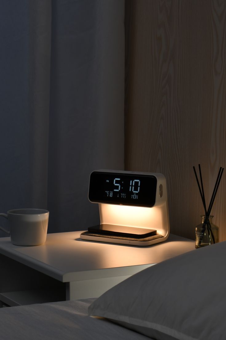 an alarm clock sitting on top of a bed next to a cup