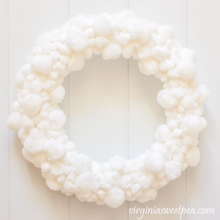 a white wreath with pom - poms hanging on the door handle, in front of a white wall