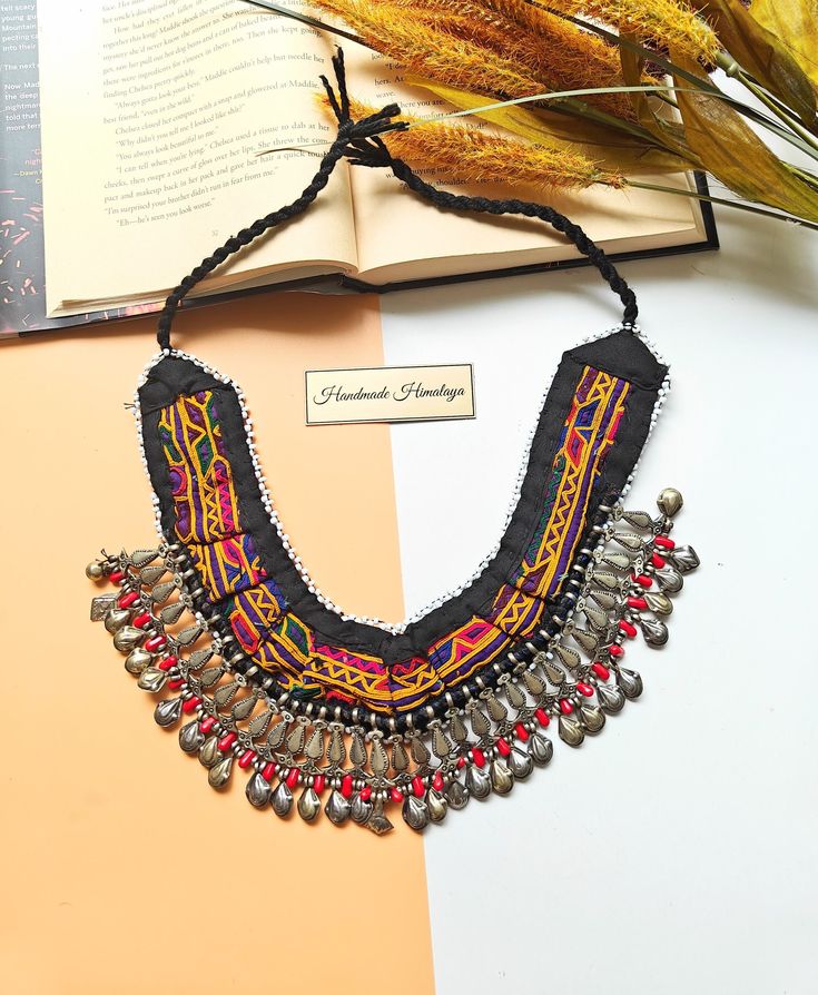 Vintage Afghan Kuchi Tribal Beaded Necklace Item Length: 8 inches approx without chord Item Weight: 4-6 oz. approx Color: Multicolor Qty: 1 The necklace is recreated using vintage materials. These materials are quite old, but artisans put them together to give us something of meaning and a unique design. The necklace comprises Kuchi tribal fabric, and bells are also from the same group.  Keeping your jewerly clean and dry is essential to preserving its natural beauty and longevity. Gently maintain its condition by using a damp cloth to clean it. Ensure you thoroughly dry it after each use. We recommend avoiding chemicals or detergents, as the organic materials used in these items are best cared for with a gentle touch. For returns and exchanges, please read the FAQ section.  Due to digital Afghani Jewelry, Afghan Jewelry, Fabric Necklace, Vintage Afghan, Necklace Unique, Gentle Touch, Organic Materials, Unique Necklace, Unique Necklaces