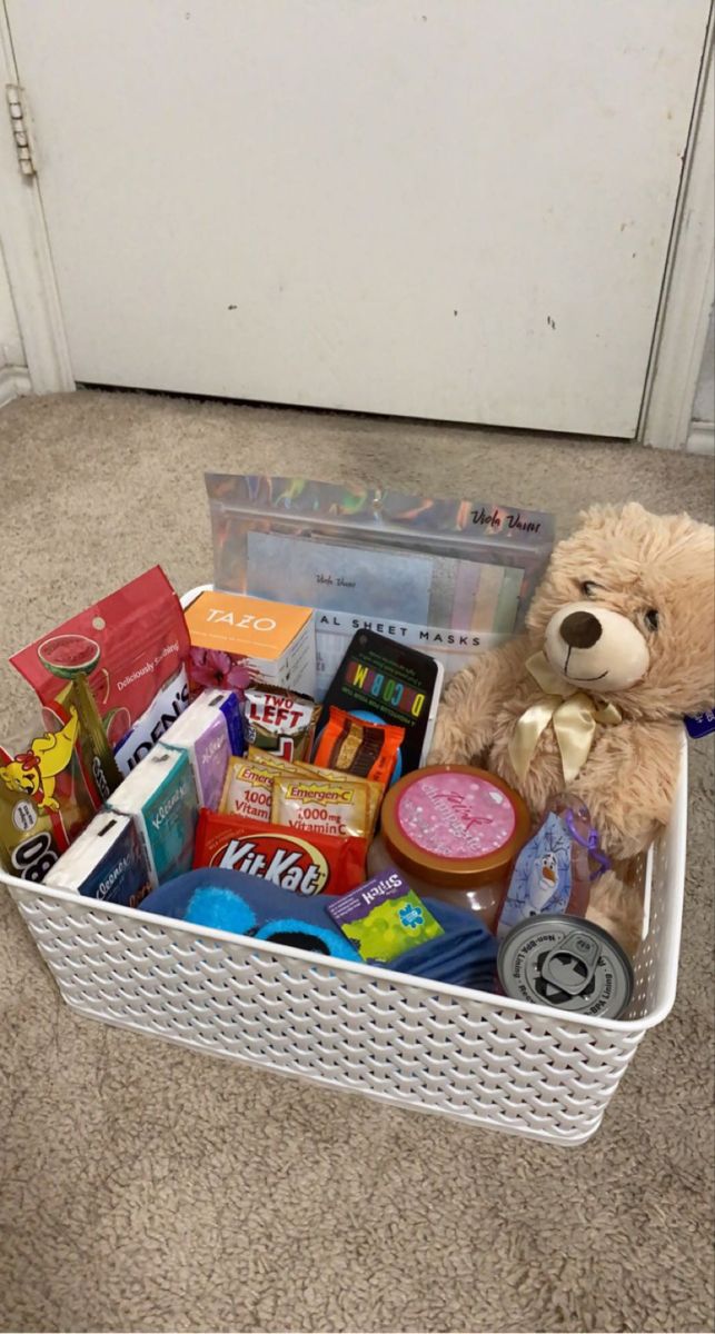 a teddy bear sitting in a white basket filled with snacks and confection items