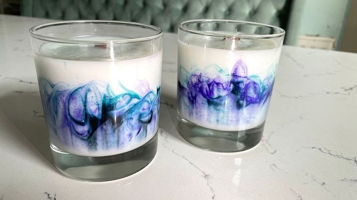 two candles sitting on top of a table next to each other with blue and purple designs