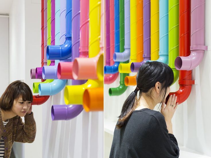 two women standing next to each other in front of rainbow colored pipes on the wall