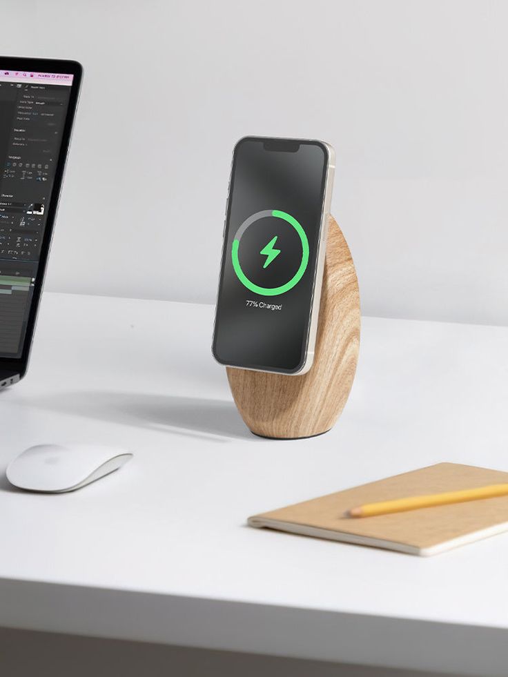 an iphone charging on a wooden stand next to a laptop computer and mouse, along with a yellow pencil